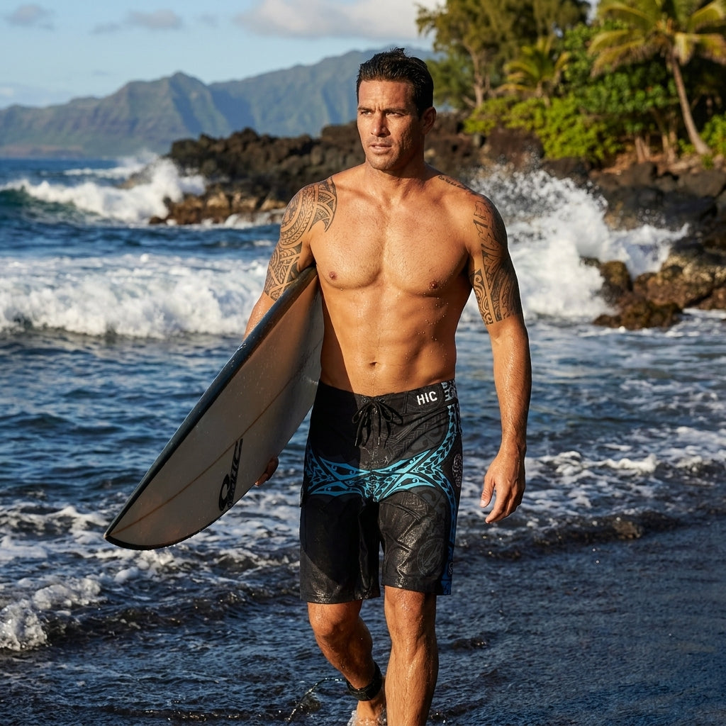 Man carrying a surfboard through shallow surf in wet HIC Kanaha black and teal board shorts, rocky shoreline and palm trees behind