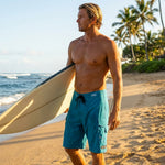Surfer in teal HIC Generals board shorts holding a surfboard on the beach