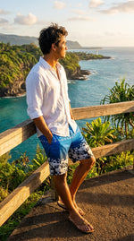 Man in a white shirt leaning on a rail above the ocean in HIC Digital Coast board shorts