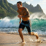 Man running along the shoreline in HIC Kanaha black and teal board shorts, wave and green mountains behind