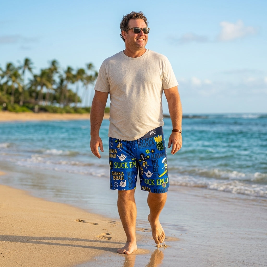 Man in a white T-shirt and sunglasses walking the shoreline in HIC Suck Em Up board shorts