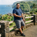 HIC Mauna Kea men's cargo walking shorts in Charcoal with a navy tee at a stone-wall ocean overlook