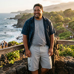 Man in HIC Mauna Kea Stone cargo walking shorts and a dark aloha shirt at a Hawaii coastal overlook