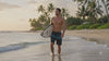 Short video of a surfer walking along the shoreline at sunset carrying a surfboard in HIC Kanaha black and teal board shorts, with a close-up of the print