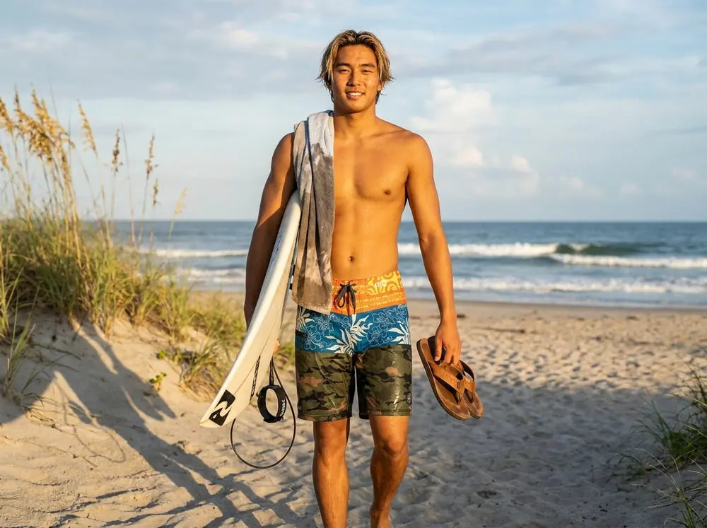 Surfer walking up the beach in HIC Ua Huka board shorts, carrying a surfboard